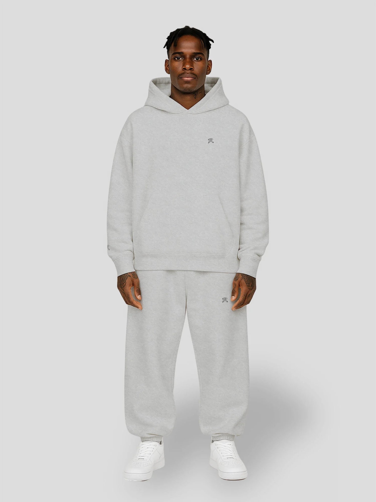 Dark-skinned male model wearing a matching grey streetwear hoodie and baggy sweatpants bundle — REMNANT. Bundles Collection product image