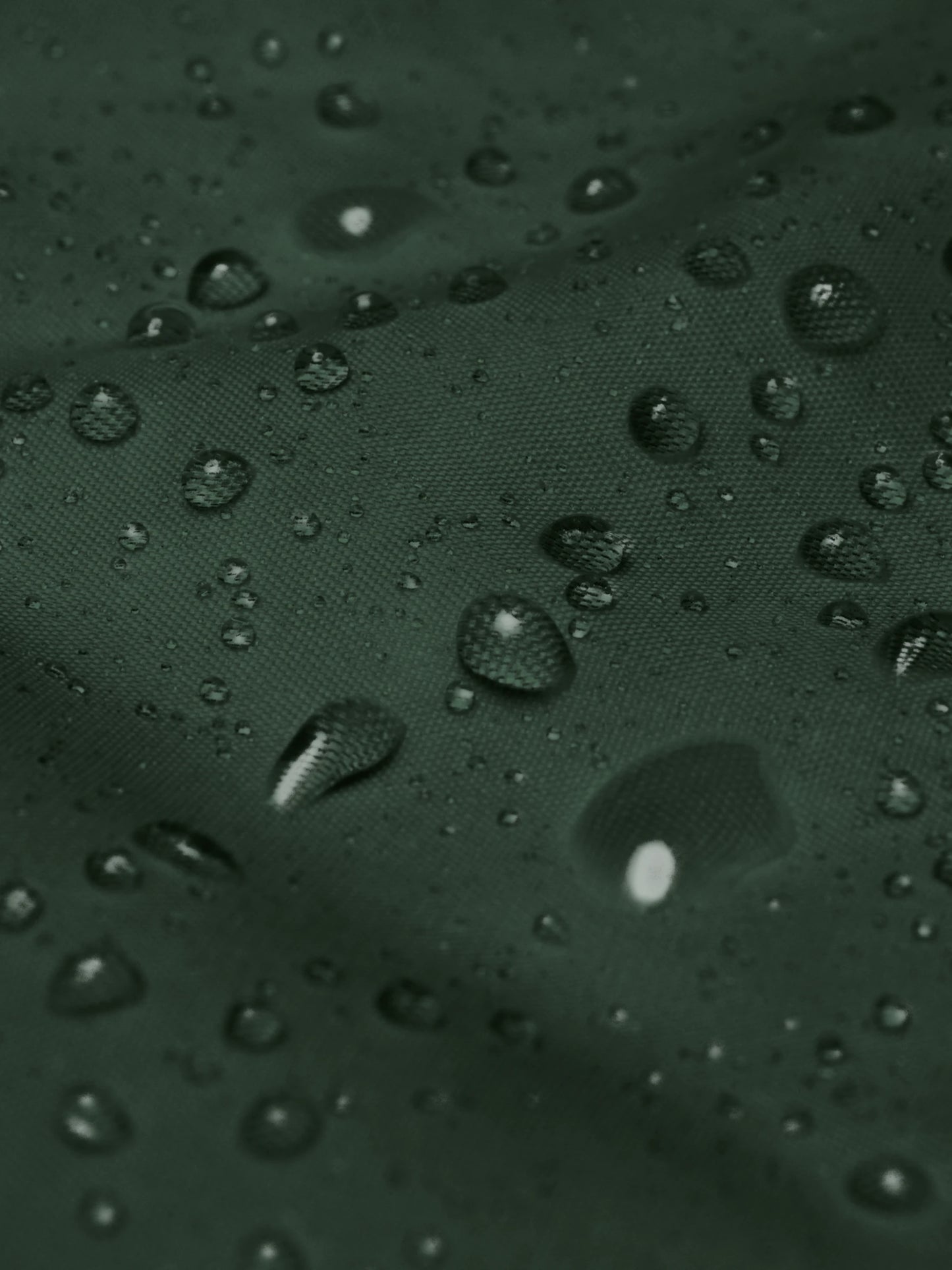 Waterproof fabric close-up showing droplets on the forest green minimalist windbreaker jacket – PETA-approved vegan outerwear.
