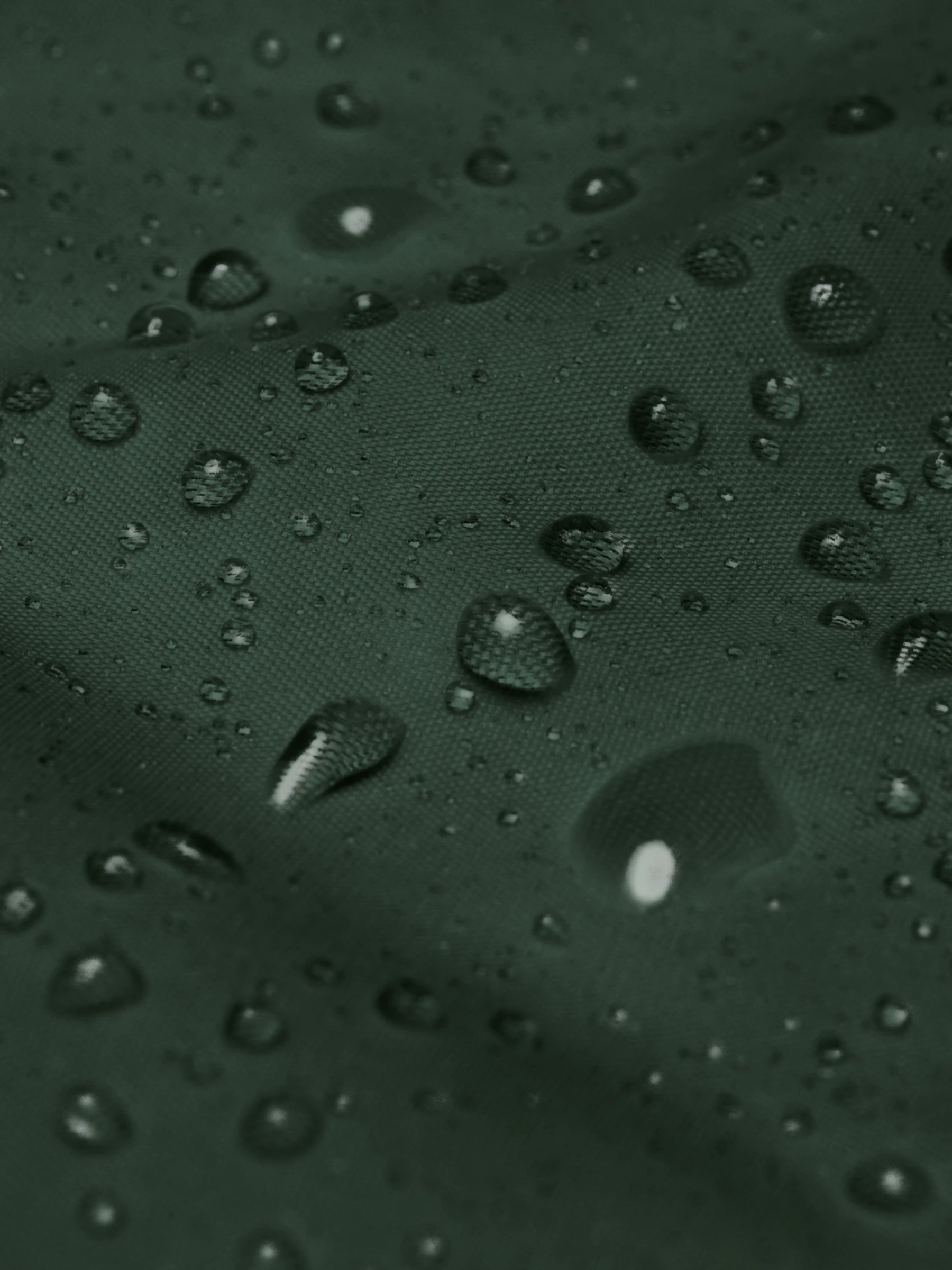 Waterproof fabric close-up showing droplets on the forest green minimalist windbreaker jacket – PETA-approved vegan outerwear.