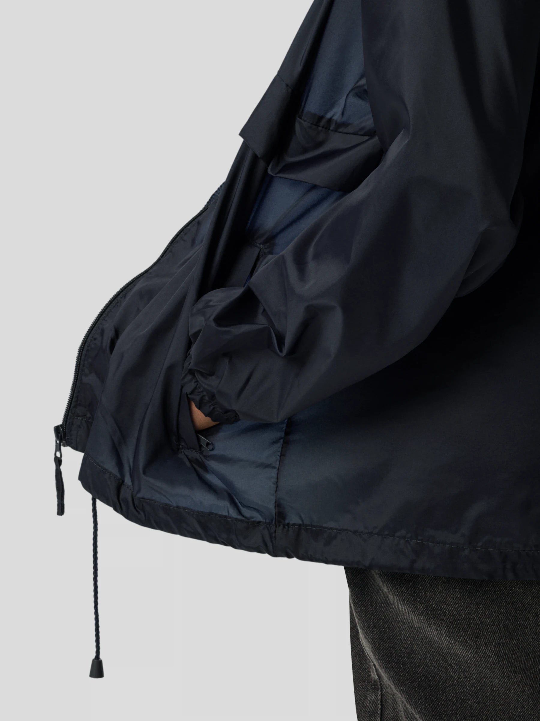 Detailed shot of the navy blue hooded streetwear windbreaker jacket pocket and adjustable drawstring hem.