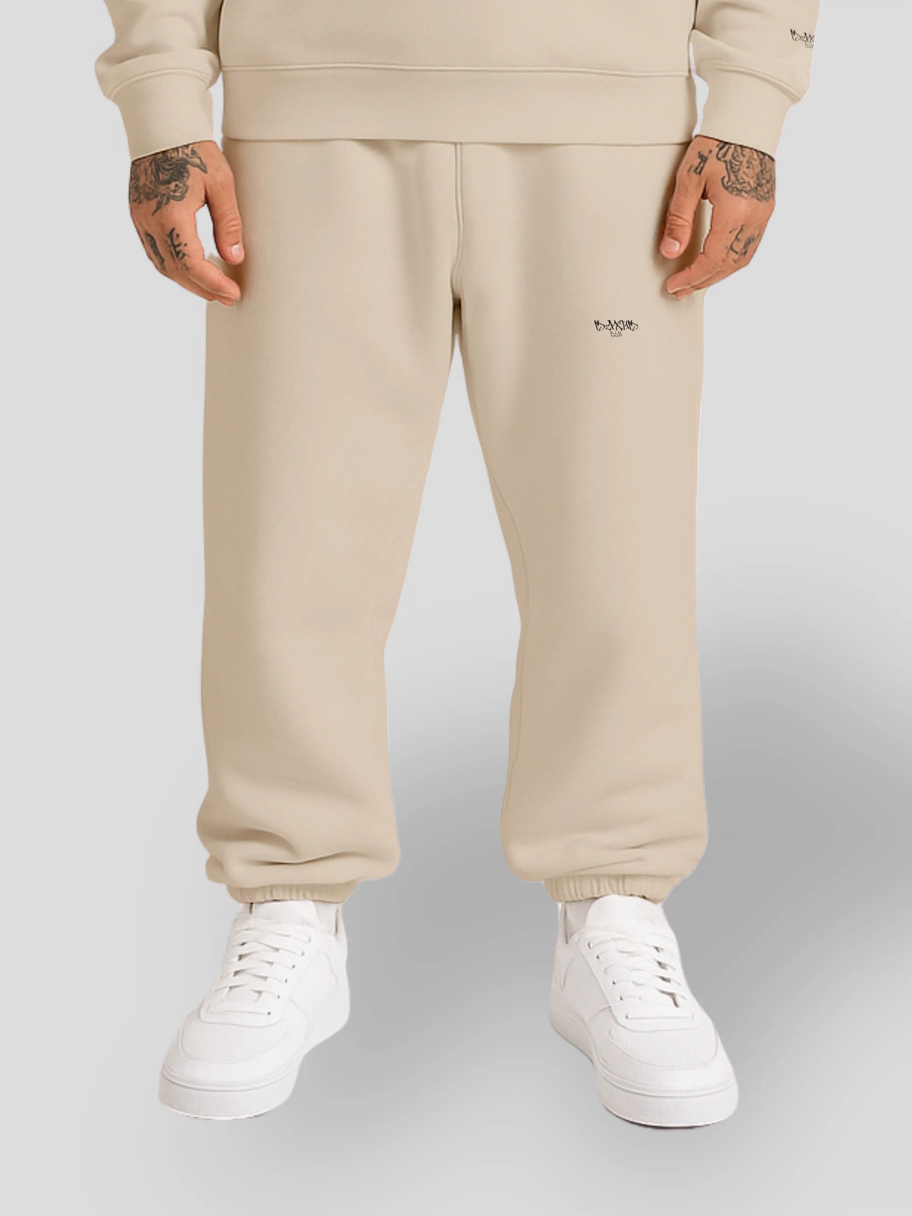 Model wearing luxury streetwear fleece sweatpants in beige — featuring a relaxed baggy fit, minimalist embroidered logo, and urban street style inspired by 90s vintage oversized joggers. A unisex premium fleece jogger from the matching sweatshirt and sweatpants set by MAXOMclo.