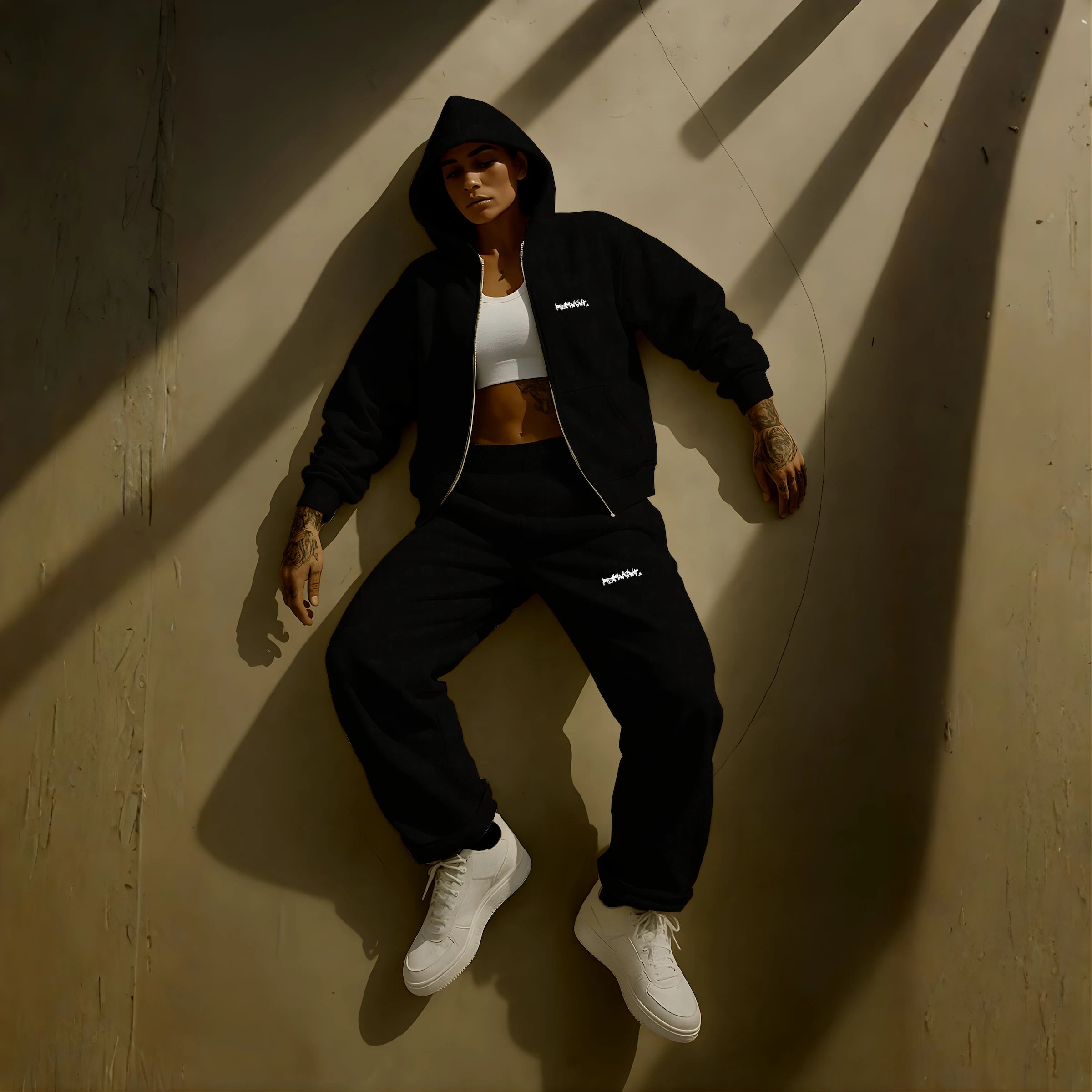 Female model wearing REMNANT. ECLIPSE_R0 black oversized streetwear set – heavyweight zip hoodie and baggy sweatpants with motivational graffiti logos, styled lying in dramatic shadow lighting for a bold urban editorial look.